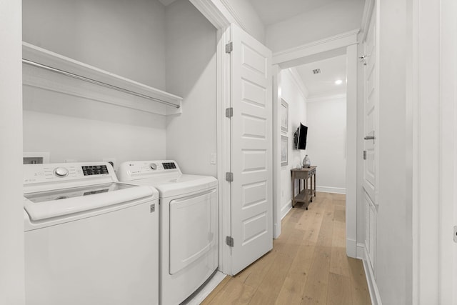 laundry area featuring ornamental molding, washer and clothes dryer, and light hardwood / wood-style flooring