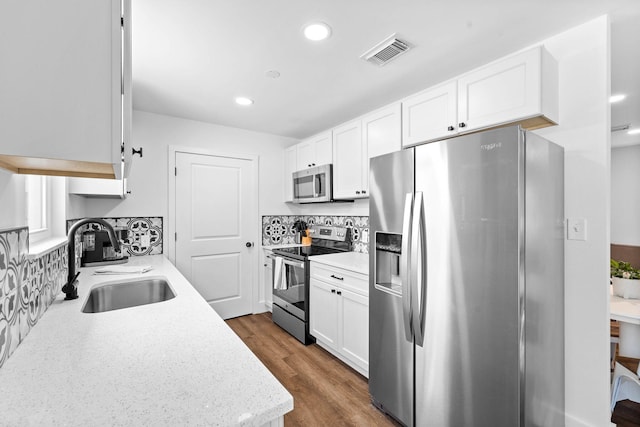 kitchen featuring white cabinetry, appliances with stainless steel finishes, decorative backsplash, light stone countertops, and sink