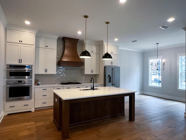 kitchen with an inviting chandelier, an island with sink, stainless steel appliances, custom range hood, and sink