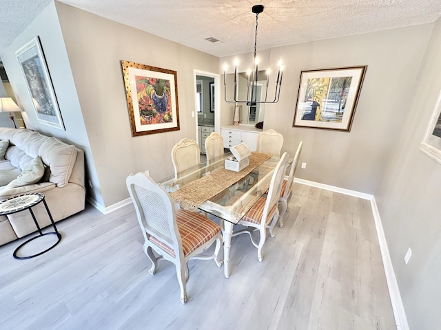 dining area with a textured ceiling, an inviting chandelier, and light hardwood / wood-style floors