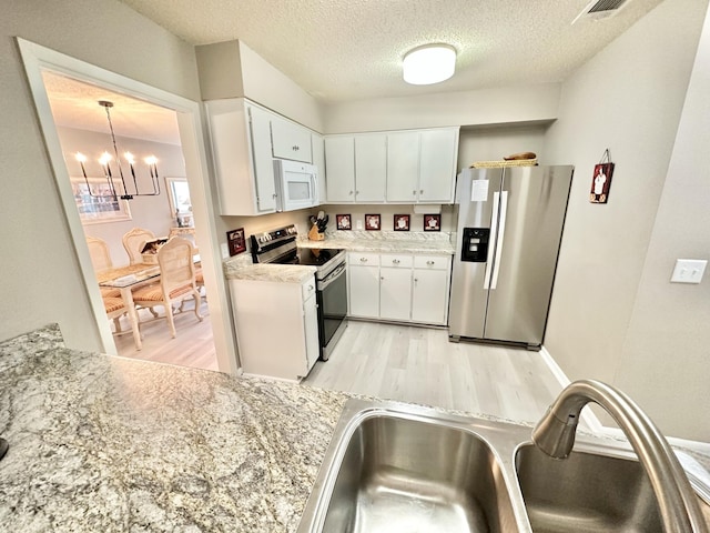 kitchen with a textured ceiling, white cabinetry, stainless steel appliances, hanging light fixtures, and a chandelier