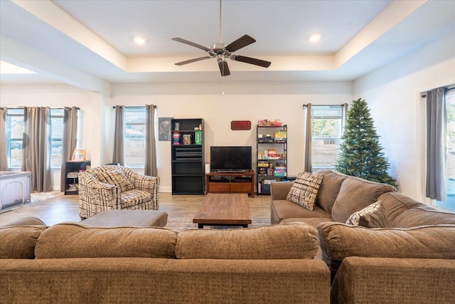 living room with a raised ceiling, ceiling fan, and light hardwood / wood-style flooring