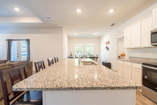 kitchen featuring white cabinetry, a kitchen bar, stainless steel appliances, and a center island with sink