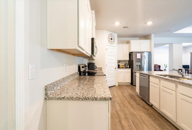 kitchen with sink, light hardwood / wood-style flooring, stainless steel appliances, light stone countertops, and white cabinets