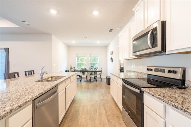 kitchen with stainless steel appliances, a kitchen bar, light stone countertops, and white cabinets