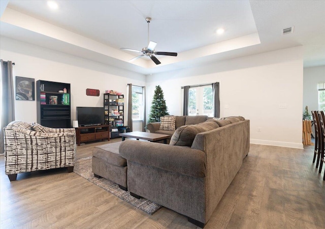 living room featuring a raised ceiling, ceiling fan, and light wood-type flooring