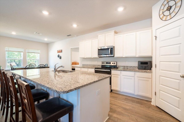 kitchen featuring sink, stainless steel appliances, light stone counters, white cabinets, and a center island with sink