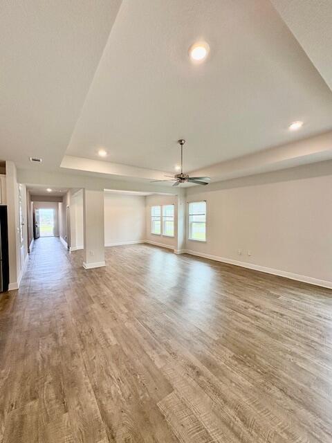 8177 Majestic Cypress Dr, Milton, FL 32583 - unfurnished living room featuring a ceiling fan, a tray ceiling, baseboards, and wood finished floors