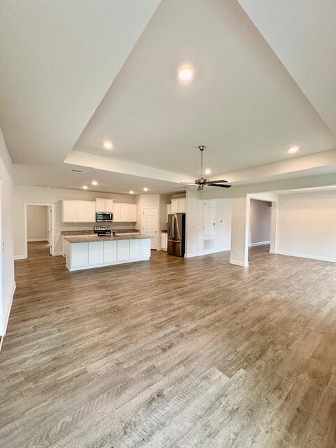 8177 Majestic Cypress Dr, Milton, FL 32583 - unfurnished living room featuring a tray ceiling, recessed lighting, baseboards, a sink, and wood finished floors