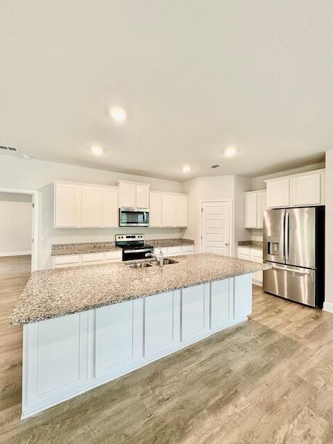 8177 Majestic Cypress Dr, Milton, FL 32583 - kitchen with white cabinetry, a large island with sink, light wood-style floors, and stainless steel appliances