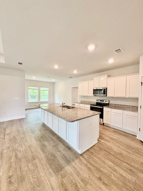 8177 Majestic Cypress Dr, Milton, FL 32583 - kitchen featuring light stone counters, light wood finished floors, visible vents, white cabinets, and appliances with stainless steel finishes