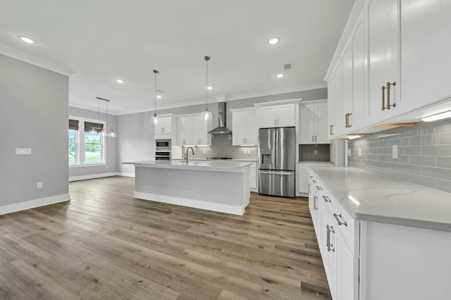 kitchen with wall chimney range hood, white cabinetry, hanging light fixtures, a kitchen island with sink, and appliances with stainless steel finishes