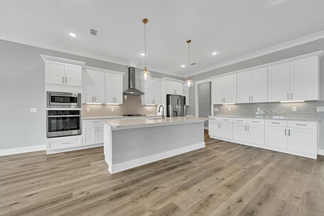 kitchen with decorative light fixtures, wall chimney range hood, white cabinetry, an island with sink, and stainless steel appliances