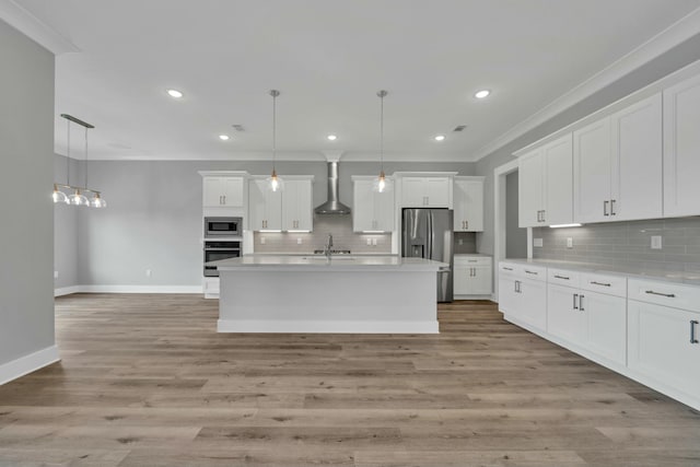 kitchen featuring stainless steel appliances, wall chimney exhaust hood, white cabinets, and hanging light fixtures