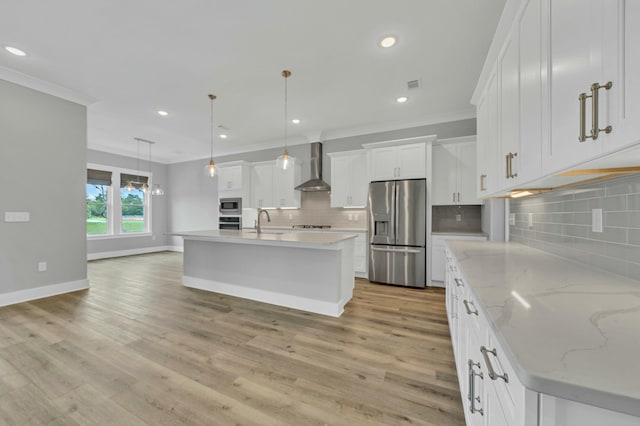 kitchen with a kitchen island with sink, appliances with stainless steel finishes, wall chimney exhaust hood, and white cabinetry