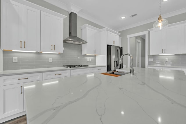 kitchen featuring light stone countertops, appliances with stainless steel finishes, ornamental molding, white cabinets, and wall chimney exhaust hood