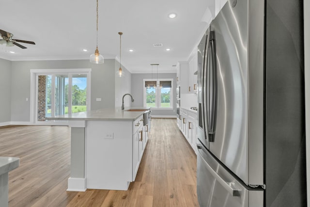 kitchen with pendant lighting, white cabinetry, stainless steel fridge, ornamental molding, and a kitchen island with sink