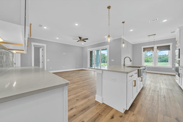 kitchen with pendant lighting, white cabinetry, ornamental molding, and a kitchen island with sink