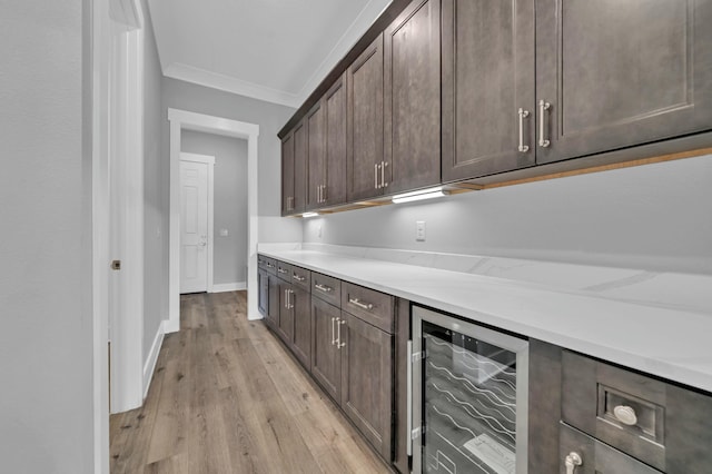 bar with light hardwood / wood-style floors, dark brown cabinets, beverage cooler, and ornamental molding