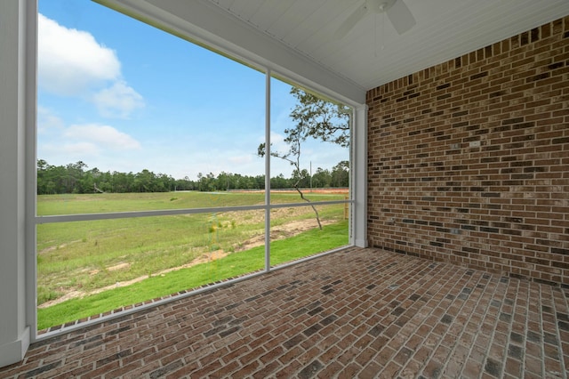 unfurnished sunroom with ceiling fan and a rural view