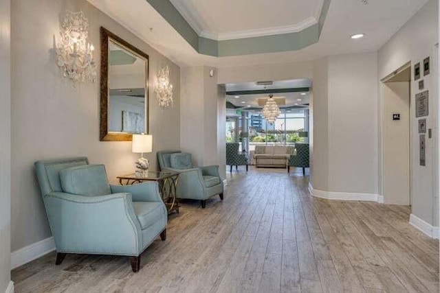 sitting room with a raised ceiling, a chandelier, ornamental molding, and hardwood / wood-style flooring