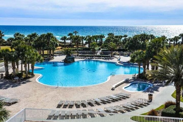 view of swimming pool featuring a hot tub, a water view, and a patio