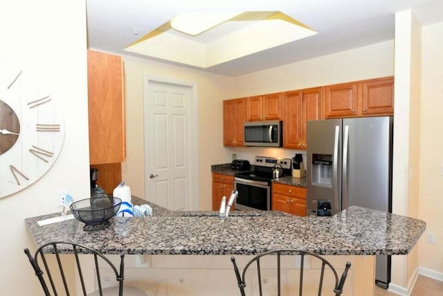 kitchen featuring kitchen peninsula, sink, a kitchen breakfast bar, stainless steel appliances, and dark stone counters