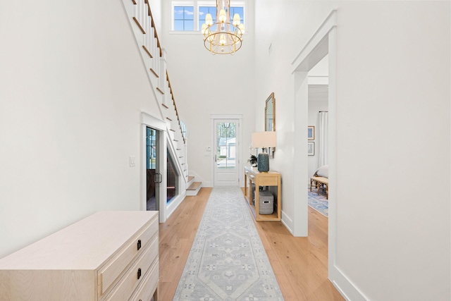 entryway with an inviting chandelier, light hardwood / wood-style floors, and a towering ceiling