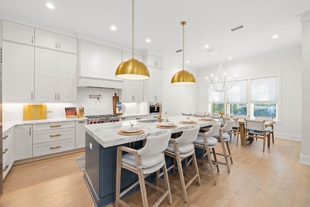 kitchen featuring a breakfast bar area, a kitchen island with sink, hanging light fixtures, white cabinets, and light stone counters