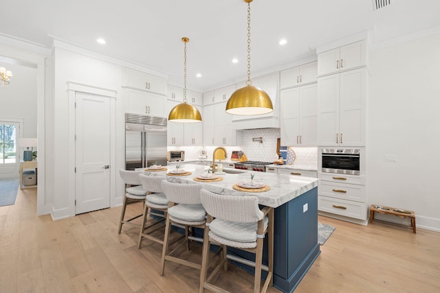 kitchen featuring white cabinetry, a kitchen bar, an island with sink, decorative light fixtures, and sink