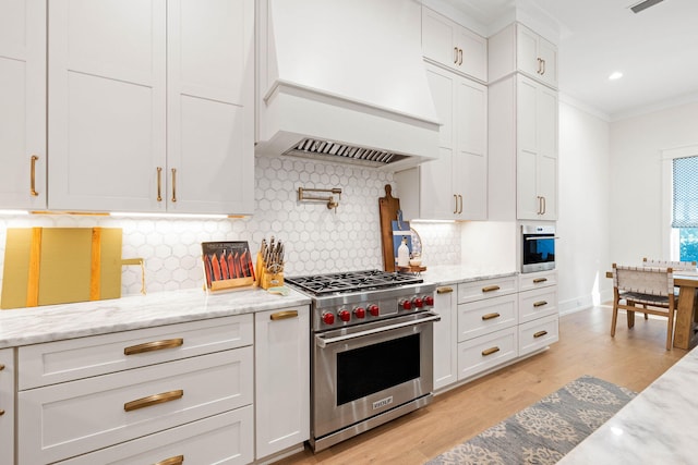 kitchen featuring backsplash, white cabinetry, appliances with stainless steel finishes, and custom range hood