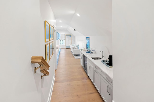 kitchen featuring dishwashing machine, white cabinets, sink, vaulted ceiling, and light hardwood / wood-style flooring