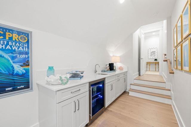 bar with light hardwood / wood-style floors, white cabinets, beverage cooler, and sink