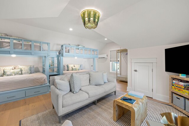 bedroom featuring a wall unit AC, lofted ceiling, and light wood-type flooring