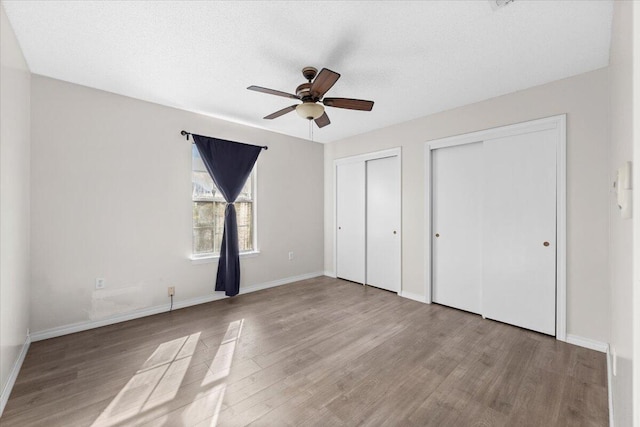 unfurnished bedroom featuring ceiling fan, multiple closets, a textured ceiling, and light hardwood / wood-style flooring