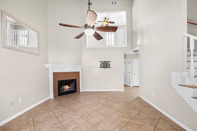 unfurnished living room featuring ceiling fan, light tile patterned floors, a towering ceiling, and a tile fireplace