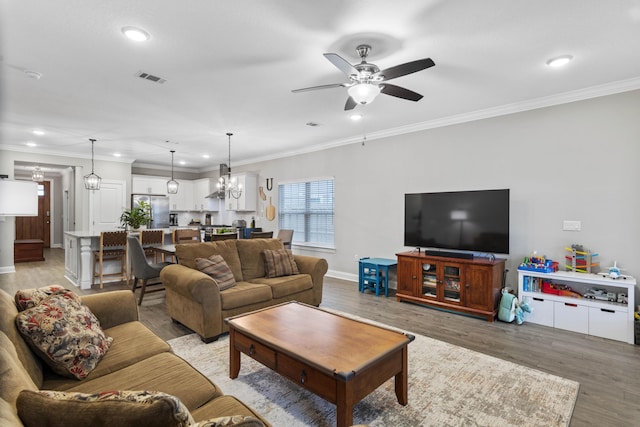 living room featuring ornamental molding, ceiling fan with notable chandelier, a wealth of natural light, and light hardwood / wood-style floors