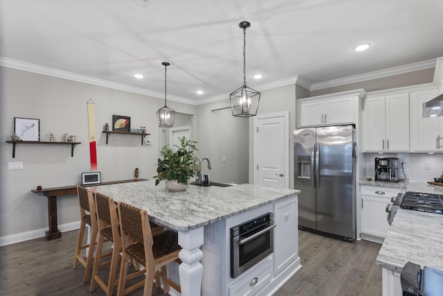 kitchen with appliances with stainless steel finishes, pendant lighting, sink, white cabinets, and a kitchen island with sink