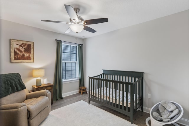 bedroom with a crib, wood-type flooring, and ceiling fan