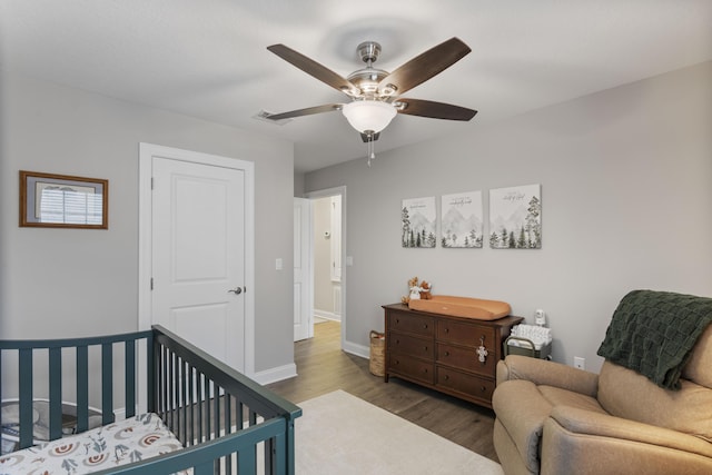 bedroom with wood-type flooring, a nursery area, and ceiling fan