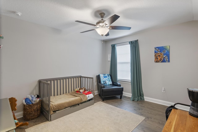 bedroom with a textured ceiling, a crib, dark hardwood / wood-style floors, and ceiling fan