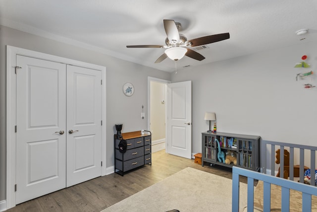 bedroom featuring a nursery area, hardwood / wood-style floors, ceiling fan, and a closet