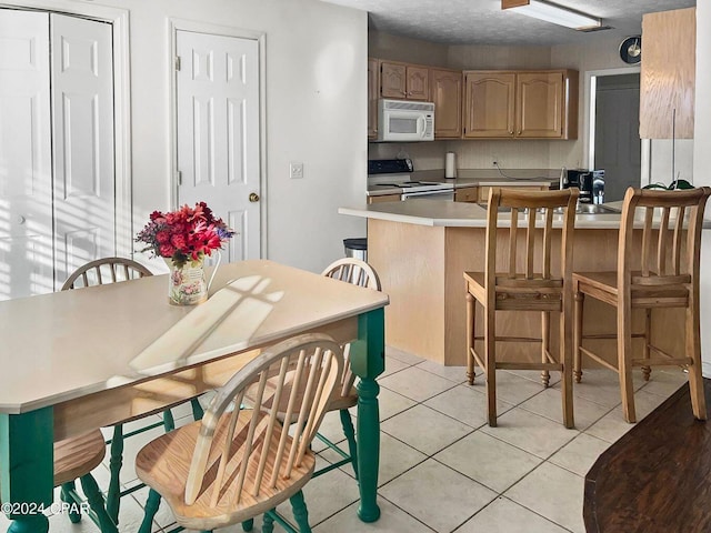 kitchen featuring white microwave, a peninsula, light tile patterned flooring, light countertops, and electric stove