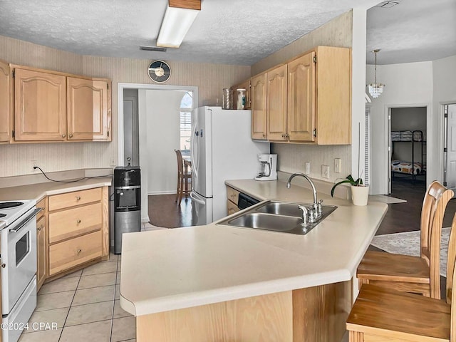 kitchen featuring light brown cabinets, a kitchen bar, a peninsula, white appliances, and a sink