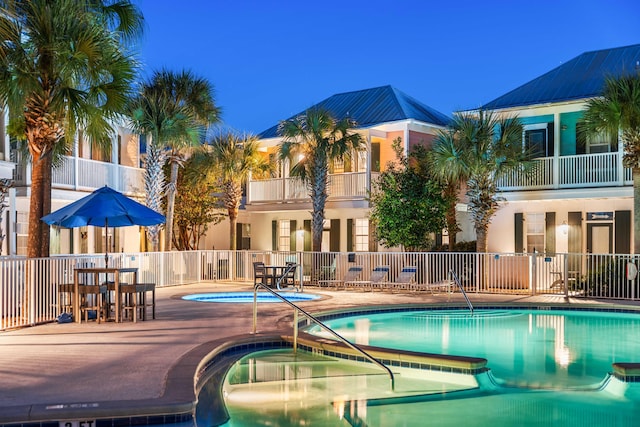 pool at dusk featuring a hot tub and a patio