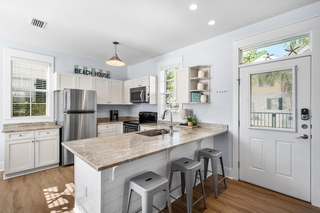 kitchen featuring appliances with stainless steel finishes, decorative light fixtures, white cabinetry, a kitchen bar, and kitchen peninsula