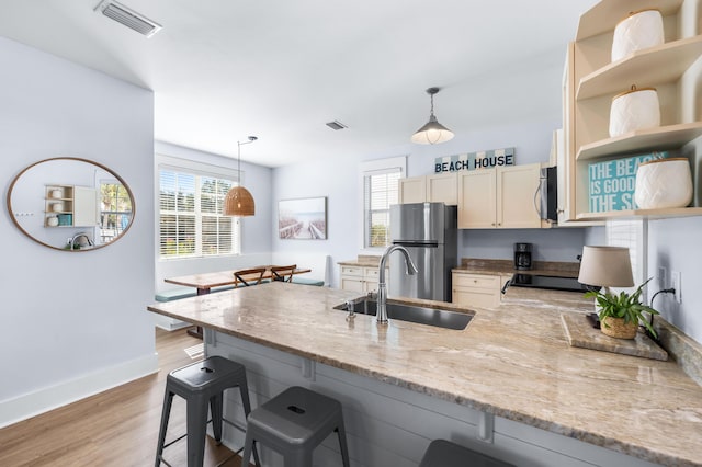 kitchen featuring sink, light hardwood / wood-style flooring, a breakfast bar, appliances with stainless steel finishes, and decorative light fixtures