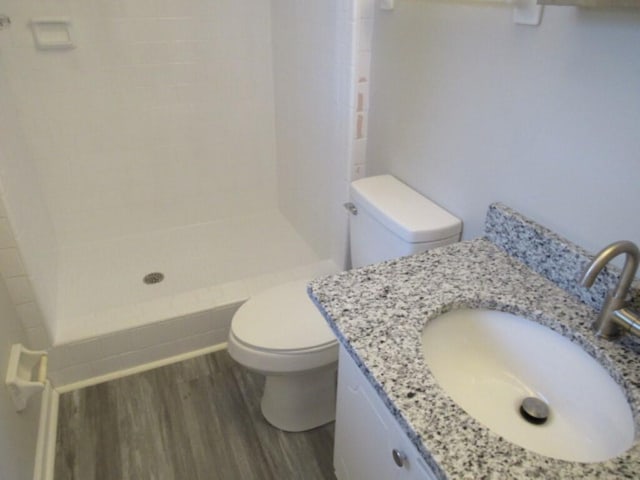 bathroom with toilet, vanity, a tile shower, and hardwood / wood-style flooring