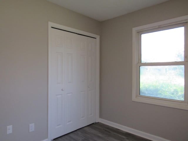 unfurnished bedroom with dark wood-type flooring, a closet, and multiple windows