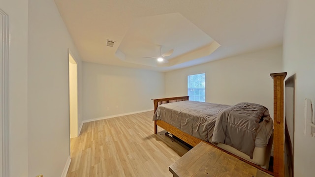 bedroom featuring ceiling fan, wood-type flooring, and a tray ceiling